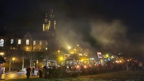 Traktoren und Landwirte stehen im Dunkeln auf einer Wiese bei St. Peter.