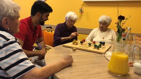 An einem Tisch spielt ein Pfleger mit den Senioren des Mitmach-Pflegeheims Rheinaue in Wyhl am Kaiserstuhl ein Spiel.