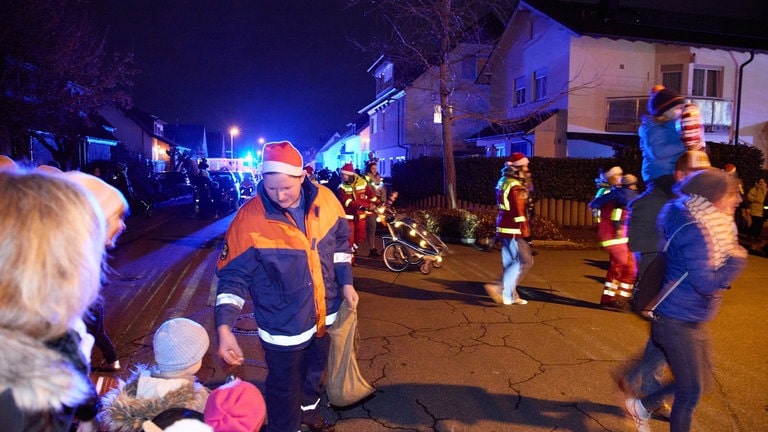 Ein Mann verteilt Süßigkeiten an Kinder, die am Straßenrand stehen beim Weihnachtscorso der Rettungskräfte