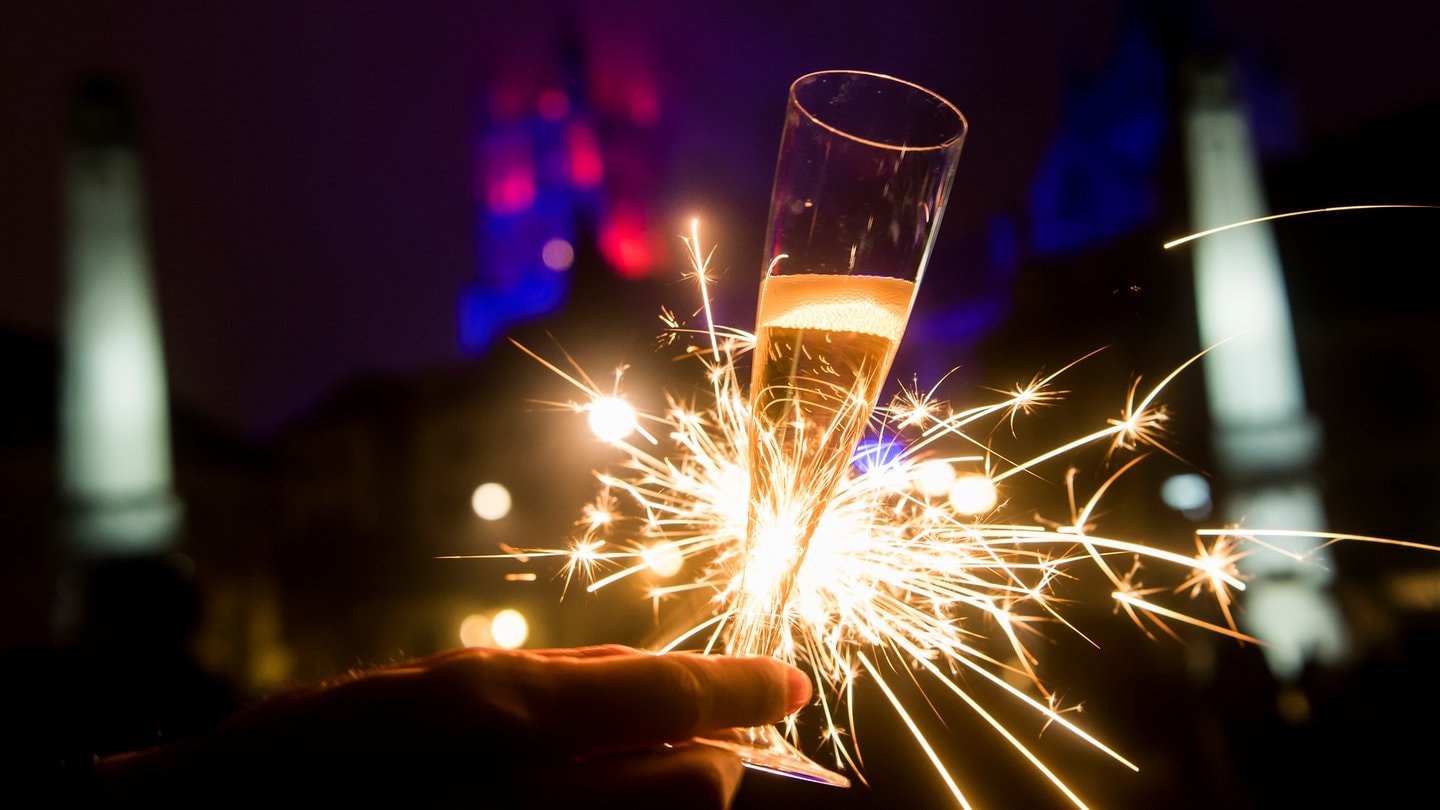 Ein Sektglas und im Hintergrund eine Wunderkerze zu Silvester.