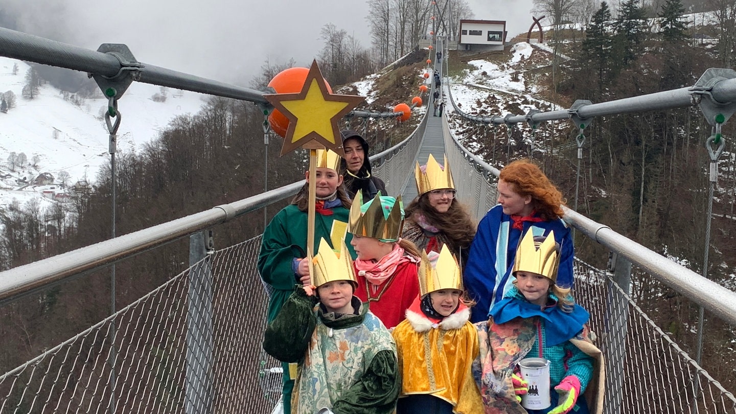 Sechs Kinder sind als Sternsinger verkleidet und singen auf der Todtnauer Hängebrücke. Im Hintergrund Schnee und Schwarzwald.