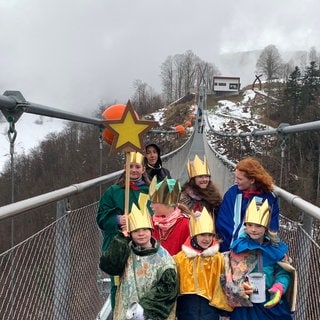 Sechs Kinder sind als Sternsinger verkleidet und singen auf der Todtnauer Hängebrücke. Im Hintergrund Schnee und Schwarzwald.