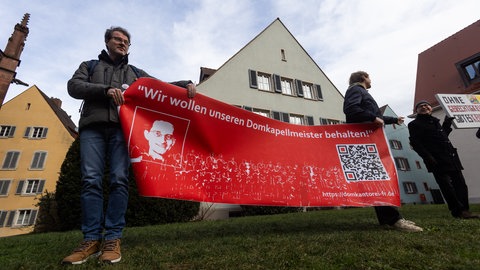 Demonstranten in Freiburg halten ein Banner mit der Aufschrift "Wir wollen unseren Domkapellmeister behalten" 