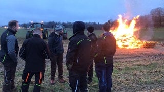 Eine Gruppe von Landwirten steht in Lahr im Ortenaukreis vor einem Mahnfeuer, das zum Jahrestag der Bauernproteste am 8. Januar angezündet wurde.