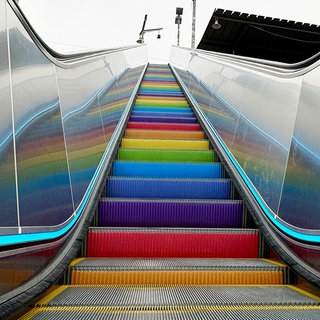 Das Bild zeigt eine Rolltreppe. Sie hat Stufen in Regenbogenfarben.