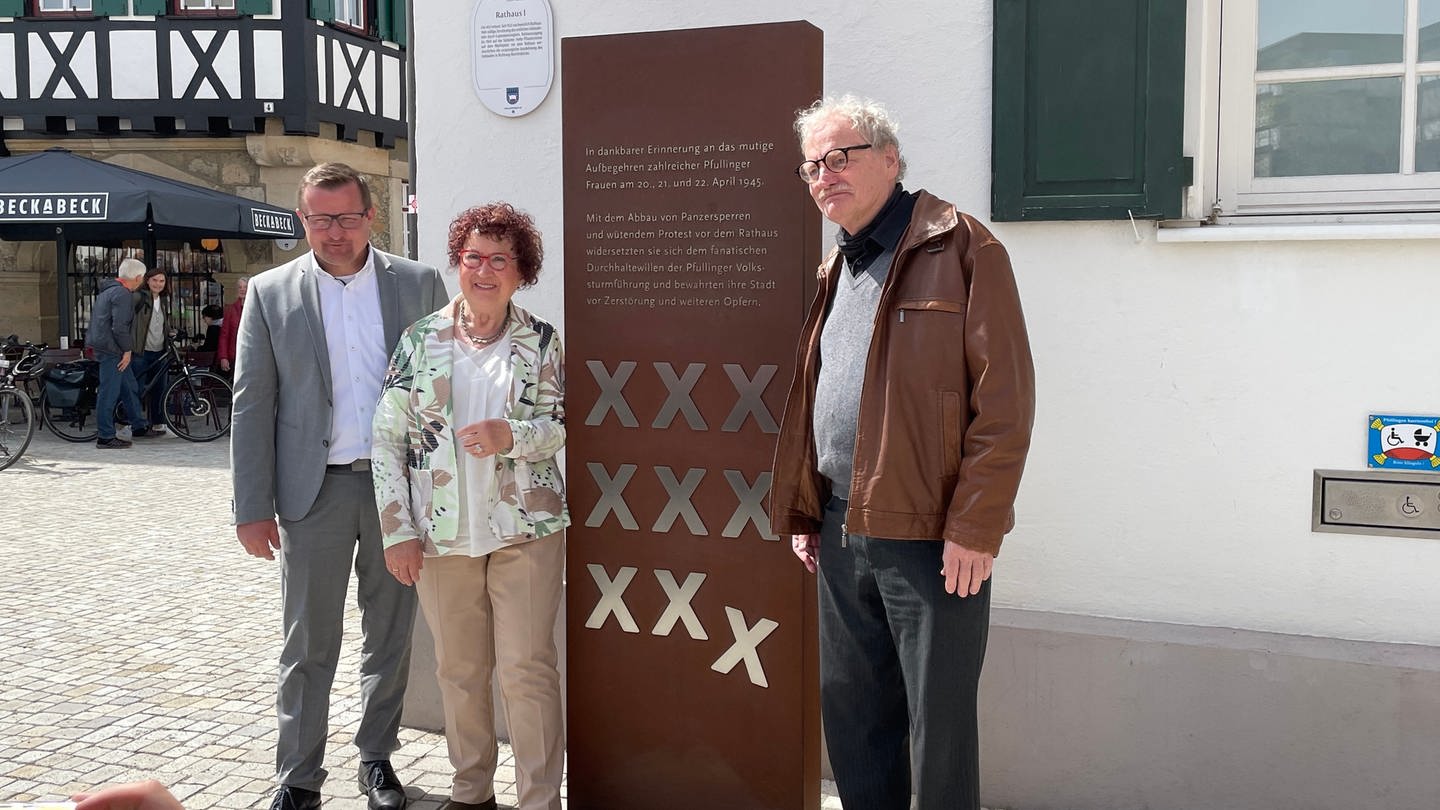 Bürgermeister, First Lady Baden Württembergs und Grafiker stehen zufrieden vor der neuen rechteckigen und übermannshohen Stele vor dem Pfullinger Rathaus.