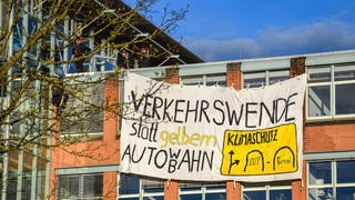 Protestplakat am Regierungspräsidium in Tübingen mit der Aufschrift: Verkehrswende statt gelbem Auto WB ahn. Mitglieder der Klimaaktivistinnen Tübingen klettern am 04.04.2024 auf das dach des Regierungspräsidiums und besfestigen ein Plakat als Protest gegen den Neubau eines B27 Tunnels 