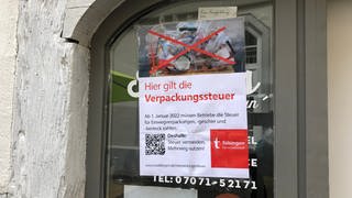 Ein Plakat der stadt Tübingen, angebracht auf einem Schaufenster, mit der Aufschrift "Hier gilt die Verpackungssteuer"