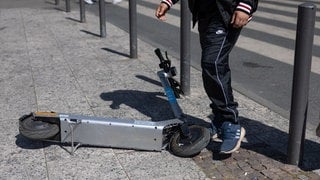 Ein Passant schiebt auf einem Gehweg einen E-Scooter zur Seite