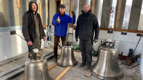 Projektleiter Johannes Längle mit Mitarbeitern der Glockengießerei Bachert stehen hinter drei neuen Kirchenglocken in Tübingen-Lustnau