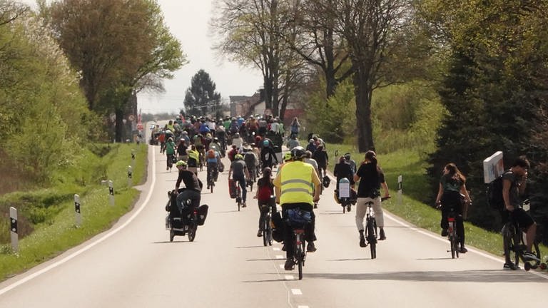 Eine große Gruppe von Radfahrenden belegt beide Spuren einer zweispurigen Straße