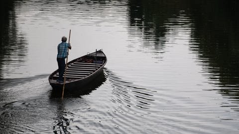 Ein Mann fährt auf dem Neckar mit einem Stocherkahn. 