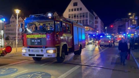 Auf der Eberhardsbrücke in Tübingen steht ein Feuerwehrauto, dessen Besatzung den Insassen eines gekenterten Stocherkahns auf dem Neckar zu helfen