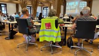 Eine Weste der Gewerkschaft ver.di hängt um einen Stuhl. Darauf sitzt eine Frau im Gemeinderat Tübingen. Sie ist Mitglied des Gemeinderats Tübingen.