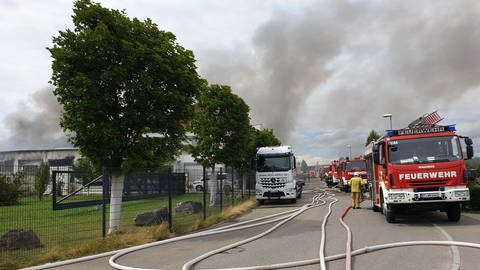 An einer Straße im Gwerbegebiet stehen ausgereit Fahrzeuge der Feuerwehren aus Walddorfhäslach und Umgebung, die bei dem Großbrand im Einsatz sind.