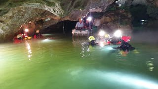 Ministerpräsident Kretschmann und Innenminister Strobl sitzen im Boot in der Wimsener Höhle und bekommen dort einen Höhlenrettungseinsatz gezeigt.