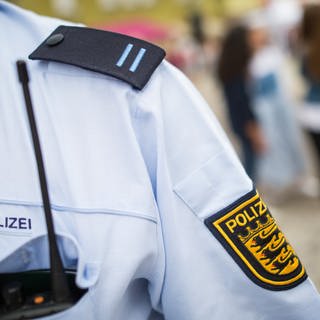 Schulterausschnitt eines Polizeibeamten bei der Streife, sichtbar sind Funkgerät, Schulterklappe und das BW-Wappen am Oberarm.