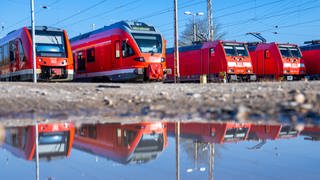 Personenzüge der Deutschen Bahn (DB) stehen auf Abstellgleisen und spiegeln sich in einer Pfütze. Mit bundesweiten Warnstreiks werden Teile des öffentlichen Verkehrs lahmgelegt.