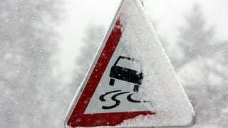 Ein schneebedecktes Verkehrsschild warnt vor Glätte.
