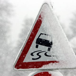 Ein schneebedecktes Verkehrsschild warnt vor Glätte.