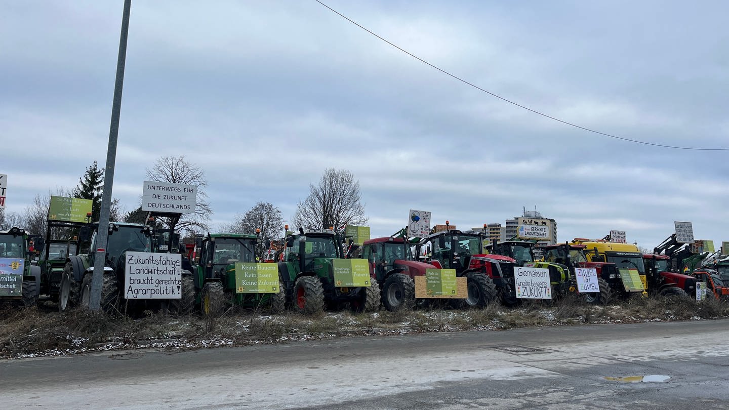 Mehrere Traktoren stehen an einer Straße geparkt. Sie präsentieren Plakate mit Sprüchen, die die Bundesregierung kritisieren.