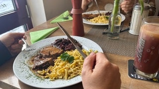 Man sieht einen Teller mit Essen. Jemand hält Gabel und Messer.