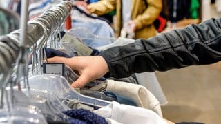 Das Foto zeigt eine Hand die nach Kleidung auf einer Kleiderstange greift. Diebe haben in Rottenburg (Kreis Tübingen) das Modehaus Weippert um mehrere hundert Hosen, Jacken und andere Markenklamotten bestohlen.