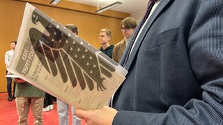 "Kepi trifft Politik" steht auf einem Blatt Papier in einer durchsichtigen Hülle des Bundestages. Im Hintergrund sind Schüler des Johannes-Kepler-Gymnasiums in Reutlingen zu sehen.