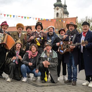 Die Narrenzunft Rälle aus Zwiefalten sammelt immer am Fasnetsfreitag Geld ein, denn die Fasnet kostet. Die Narren ziehen musizierend und singend durch den Ort. Vorne in der Mitte kniet SWR reporterin Friederike Dauser.