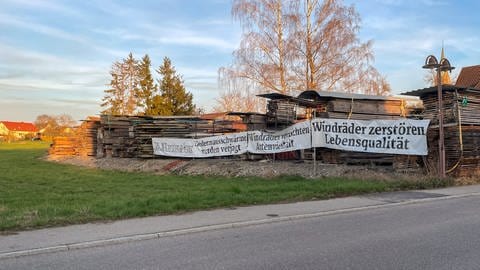 Ein Protestplakat gegen Windräder hängt neben einem Holzlager in Starzach, Kreis Tübingen. In Starzach wird ein Windpark mit sieben Windrädern geplant.
