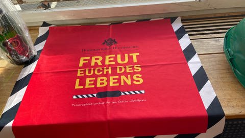 Auf einem roten Tuch mit schwarz-weißer Borte steht in gelben Buchstabden "Freut euch des Lebens", der TItel der heimlichen Hymne bei den Veranstaltungen der Fasnet in Sigmaringen.
