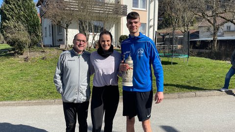 Die "Aktiven" beim Eierschupfen stehen nebeneinander. Von links: Bürgermeister und Fänger Hans Marquart, Schupferin Fabienne Villing, Läufer und Gewinner Christian Bischoff Zweiliter-Bierkrug in der Hand.