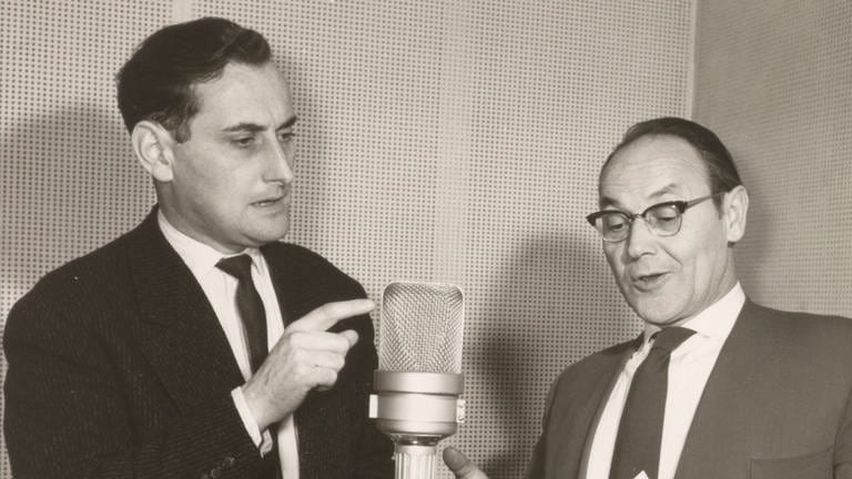 Walter Schultheiß und Eugen Morlock auf einem schwarzweiss Foto vor einem Mikrofonständer beim Einsprechen eines Hörpsiels im Aufnahmestudio.