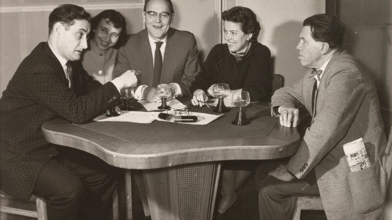 Sprecherteam im Studio, mit Walter Schultheiß (links) und vier weiteren Sprechern, die um einen runden Tisch sitzen. 