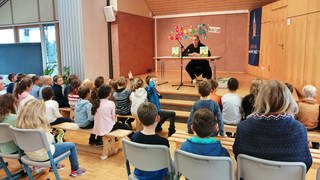 Empfingens Bürgermeister Ferdinand Truffner stellt Kinderbuch vor Erstklässlern an Grundschule vor.
