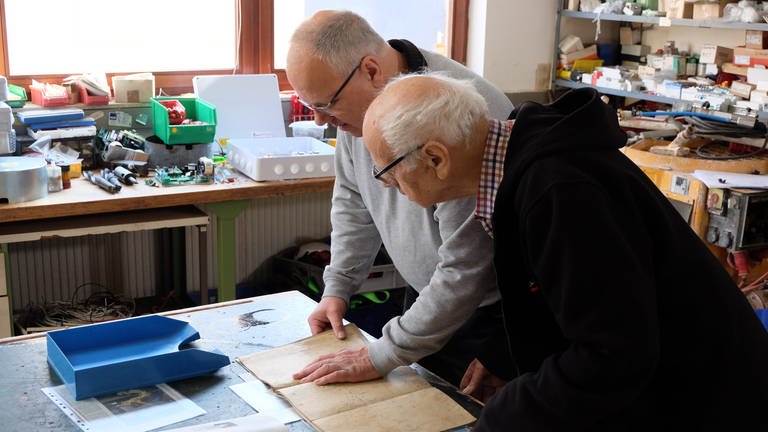 Andreas und Alfred Walz stehen in der Werkstatt und schauen sich alte Pläne der Kirchturmuhr an