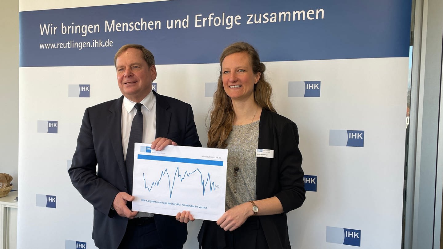 IHK-Hauptgeschäftsführer Wolfgang Epp und Antonia Hettinger, Leiterin regionale Wirtschaftspolitik halten ein Schaubild mit einer Konjunkturkurve in die Kamera.