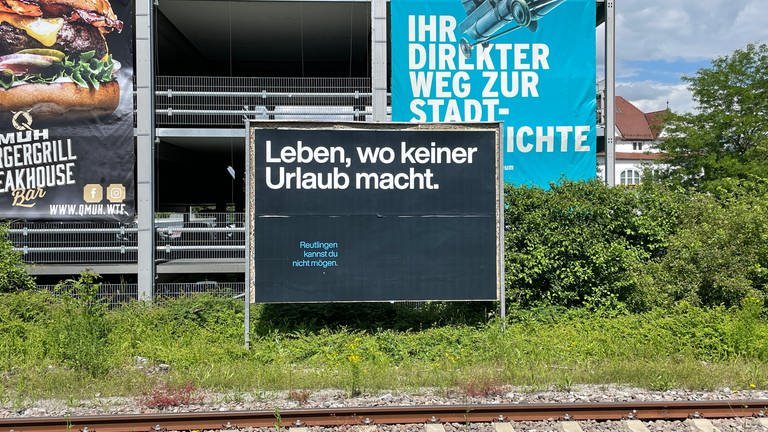 "Leben, wo keiner Urlaub macht". Dieser Spruch steht auf einem Schmäh-Plakat am Reutlinger Bahnhof.