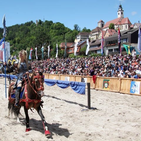 Eine blonde Frau in Rüstung auf einem fürs Turnier geschmückten Pferd vor der Kulisse der Stadt Horb, bei den Horber Ritterspielen 