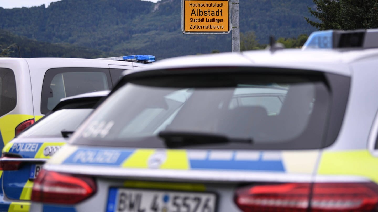 Polizei-Fahrzeuge stehen vor dem Ortsschild in Albstadt-Lautlingen. In dem Ort hat ein Mann sich und seine Schwiegermutter und seinen Sohn mit einer Waffe getötet, seine Frau und seine Tochter überlebten schwer verletzt.