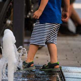 Ein kleiner Junge kühlt seine Füße in einer Wasserfontäne in der Fußgängerzone.