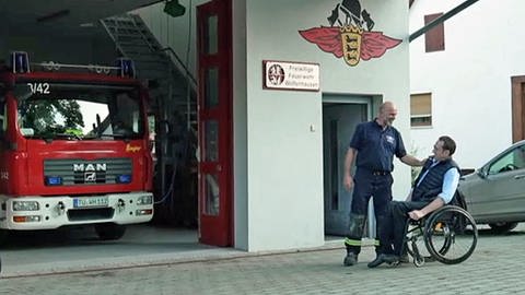 Andreas Braun im Rollstuhl und ein Feuerwehrmann vor dem Feuerwehrhaus in Neustetten-Wolfenhausen