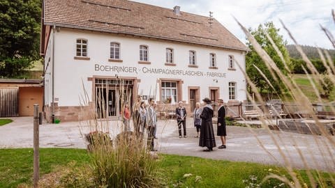 Ein historisches Gebäude, vor dem eine Besuchergruppe einer Frau in historischer Tracht lauscht.