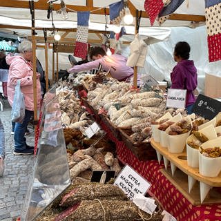 Ein Stand aus der Provence verströmt intensiven Salami-Geruch. Ein Verkäufer bedient eine Kundin. Überall hängen Frankreich-Fahnen. Beim umbrisch-provenzalischen Markt Tübingen entsteht so mit weiteren Ständen und anderen Spezialitäten ein intensiver Duft.