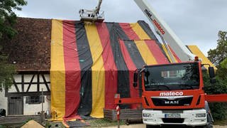 Ein Bauernhaus im Freilichtmuseum Neuhausen ob Eck ist mit einer Plane in den Deutschlandfarben verpackt