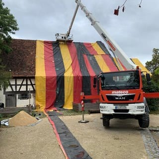 Ein Bauernhaus im Freilichtmuseum Neuhausen ob Eck ist mit einer Plane in den Deutschlandfarben verpackt