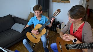 Ein 13-jähriger Junge aus Tübingen gibt einer erwachsenen Frau Gitarrenunterricht.