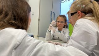 Bei "Türen auf mit der Maus" lernen Kinder in Laborkitteln und mit Schutzhauben auf an der Uniklinik Tübingen, wie pipettieren geht.