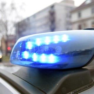 Blaulicht auf dem Dach eines Polizeiautos. Im Hintergund ist unscharf ein Wohngebiet zu erkennen.