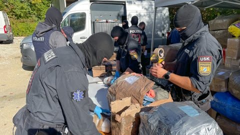 Vermummte Personen des LKA untersuchen Gegegenstände in großen Kartons, die bei einer Razzia in Reutlingen am 09.10.24 beschlagnahmt wurden.